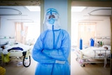 A man in full PPE leans against a pylon between two hospital rooms and closes his eyes 