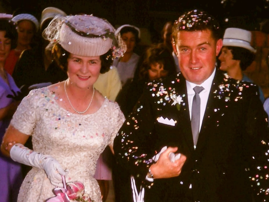 An old photo of a man and a woman smiling at the camera covered in confetti on their wedding day