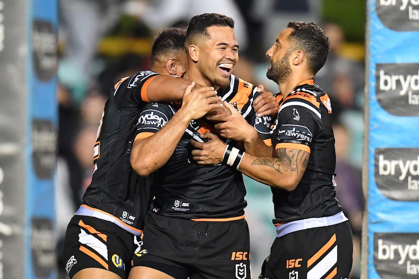 A male NRL player is hugged by two teammates after he scored a try.