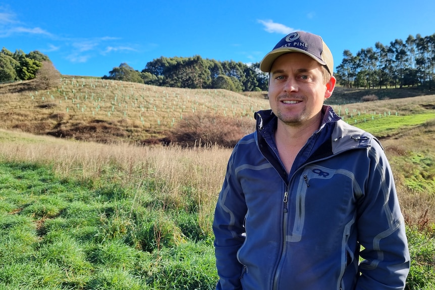A young man smiles in a green paddock on a clear blue day.