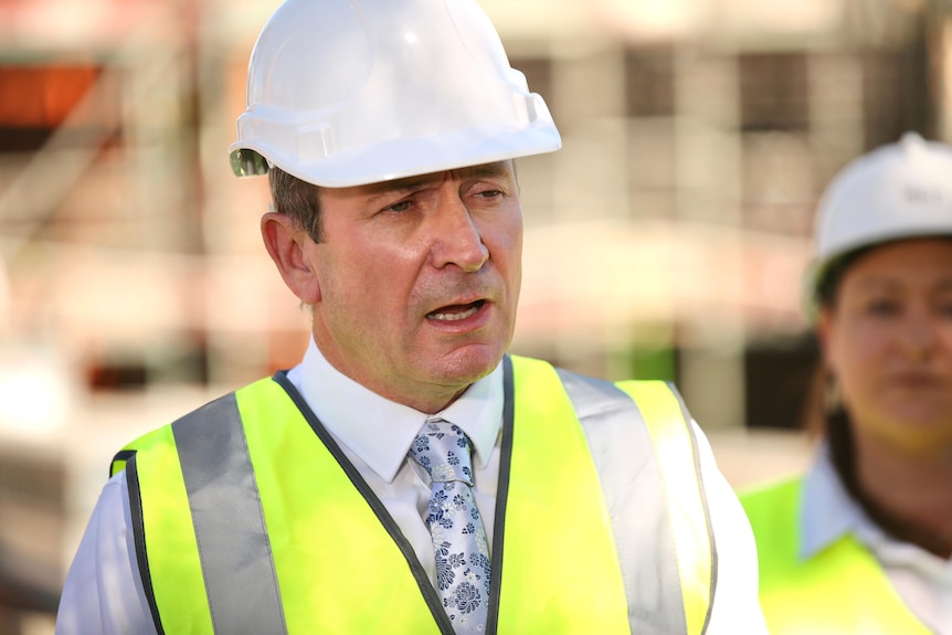 WA Premier Mark McGowan stands wearing a high-vis vest and a white hard hat. 