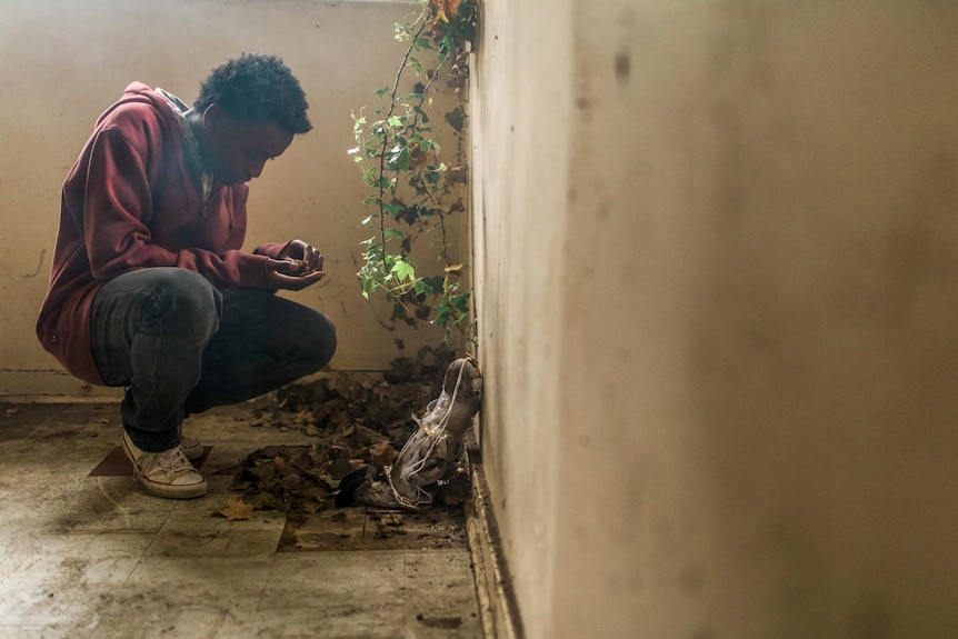 Lead actor Yared Scott crouches in a corner and sifts through leaf litter.