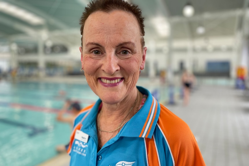 A uniformed woman smiles at the camera from outside a pool