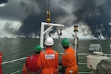 Three workers look out at smoke rising from the ocean.