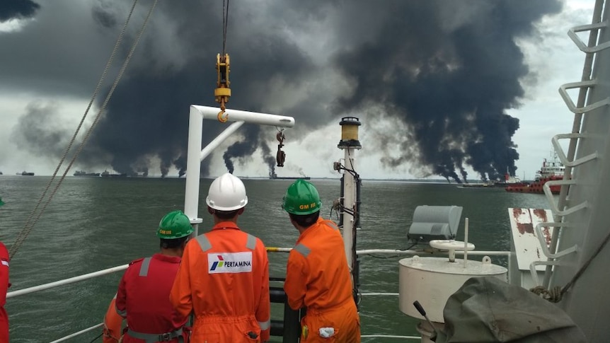 Three workers look out at smoke rising from the ocean.