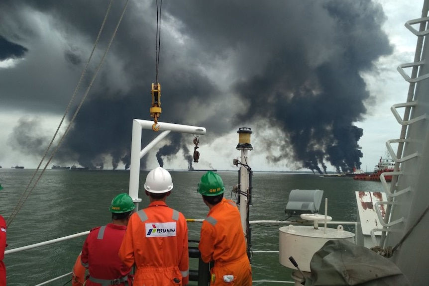 Three workers look out at smoke rising from the ocean.