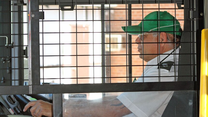 A bus driver sits in the driver's seat behind a cage door.