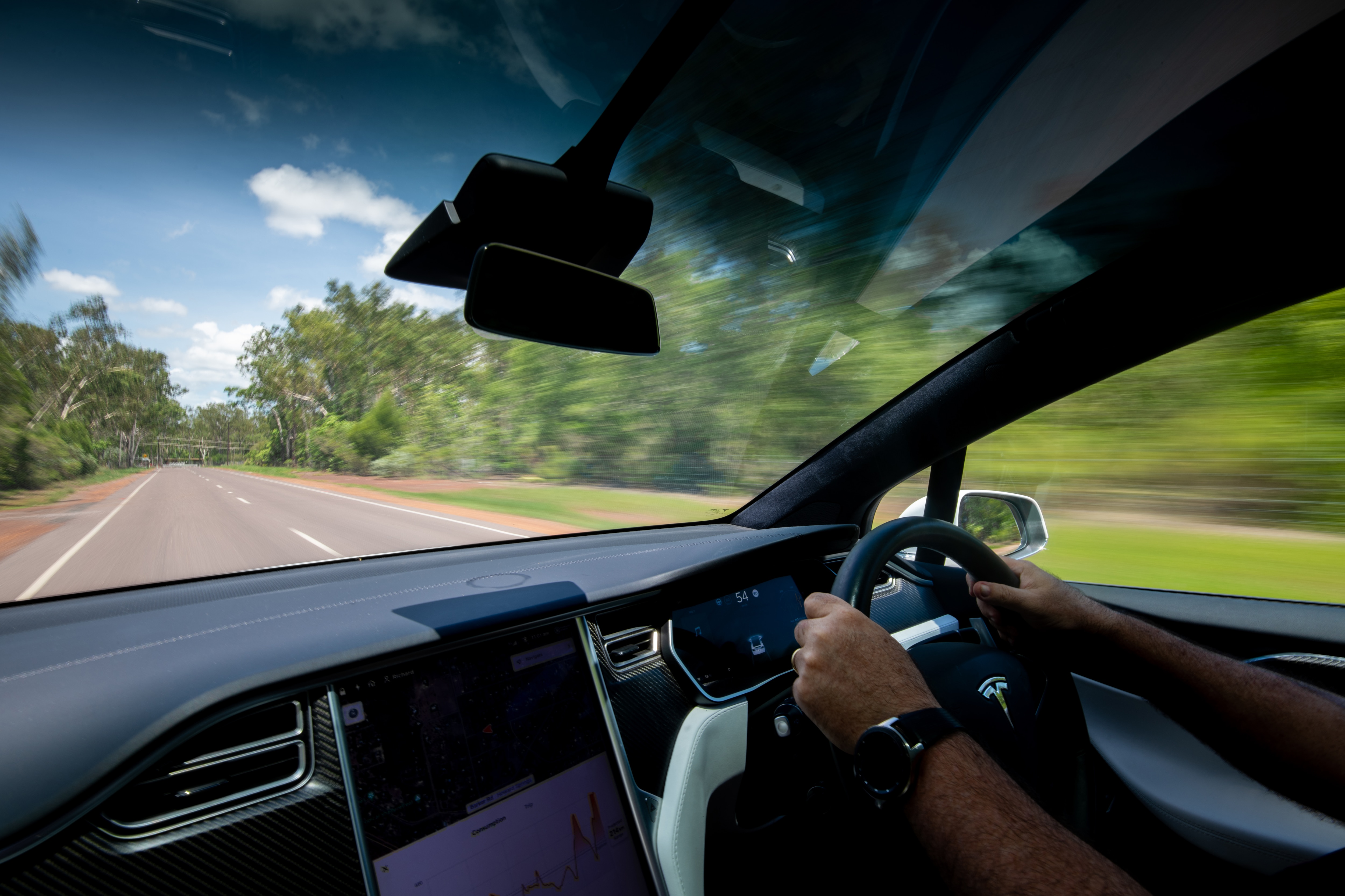 A view of a person's hands holding the steering wheel of a car and the road out the front windscreen.