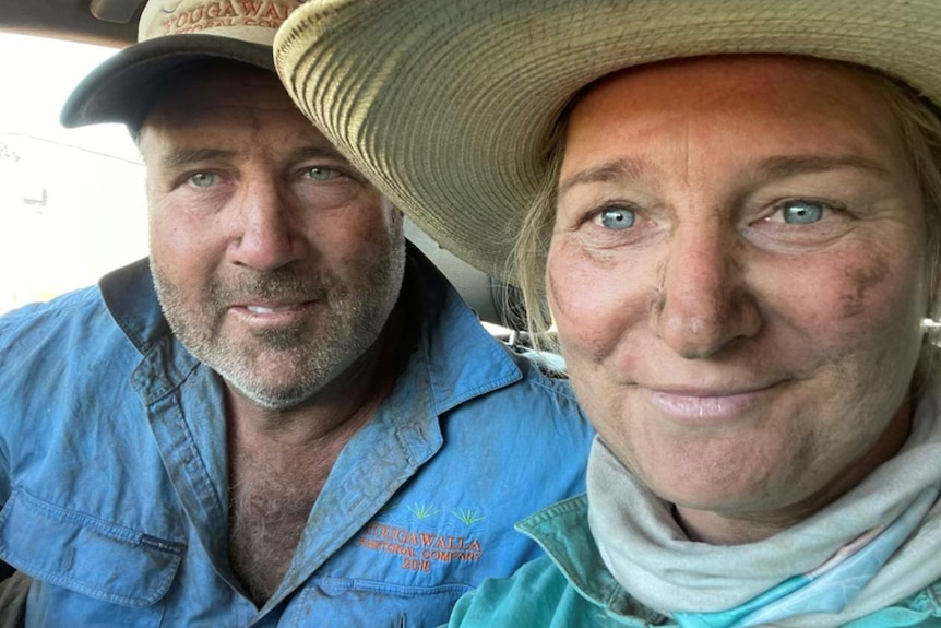 A man and a woman wearing blue work clothes take a close up of their faces. 