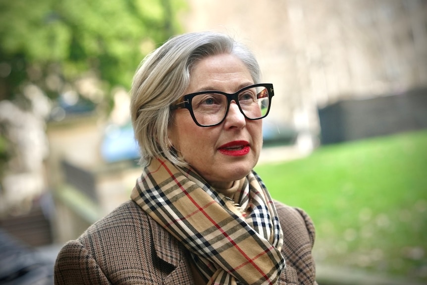 a woman with short hair and glasses looks to the right of the frame