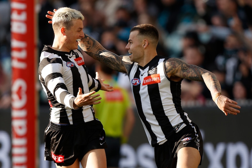 Jack Ginnivan and Jamie Elliott of the Collingwood Magpies run and hug during an AFL game.