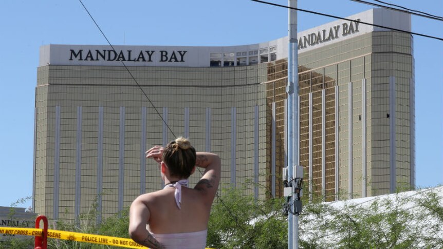 A lady looks past police tape up at the Mandalay Bay hotel with broken windows.