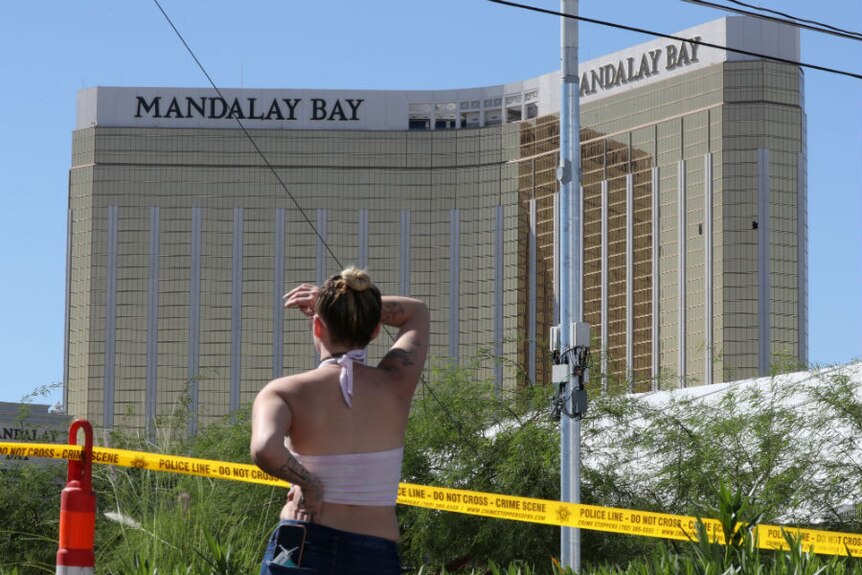A lady looks past police tape up at the Mandalay Bay hotel with broken windows.