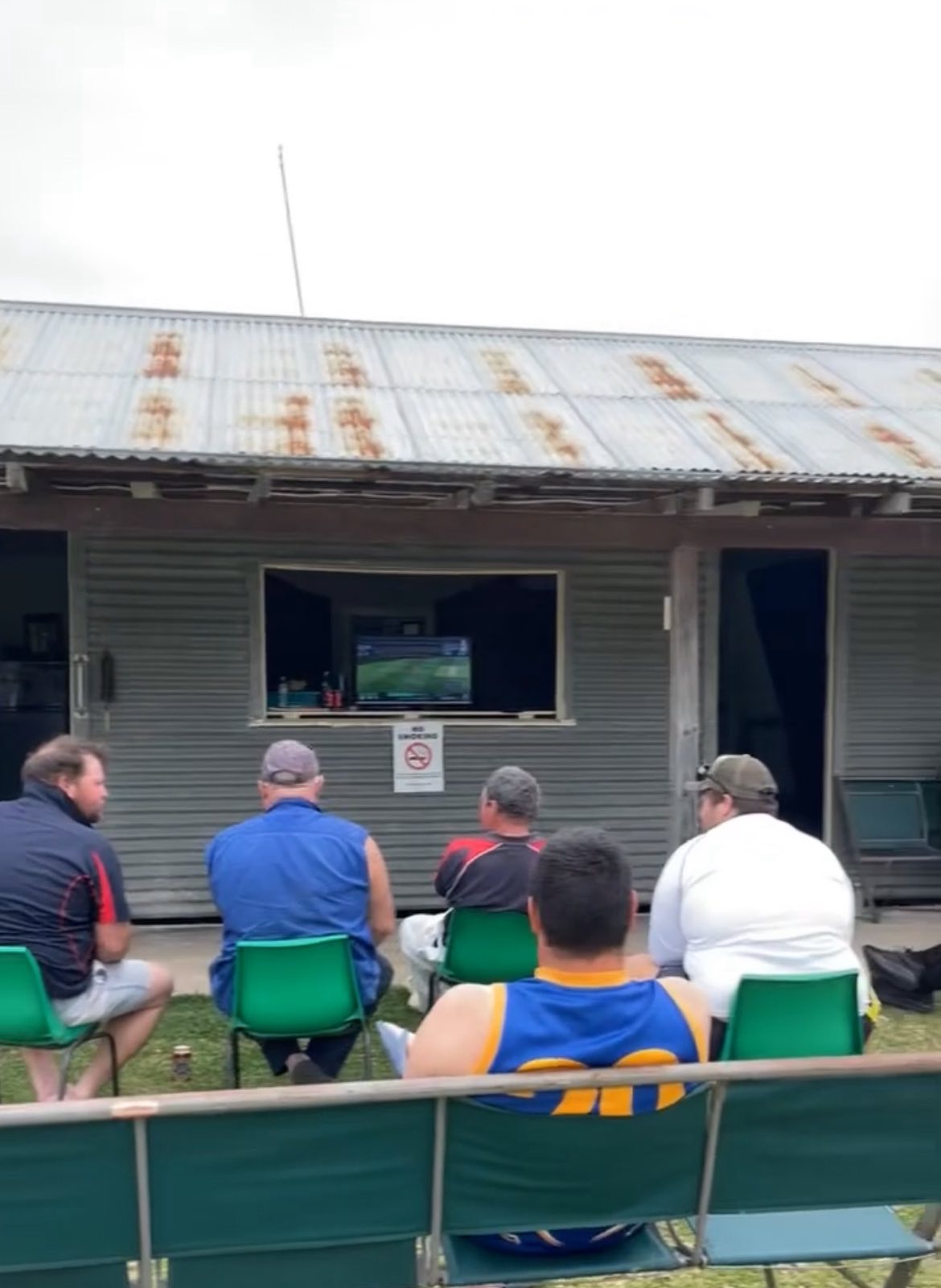 Un grupo de hombres está viendo cricket en un pequeño televisor afuera.