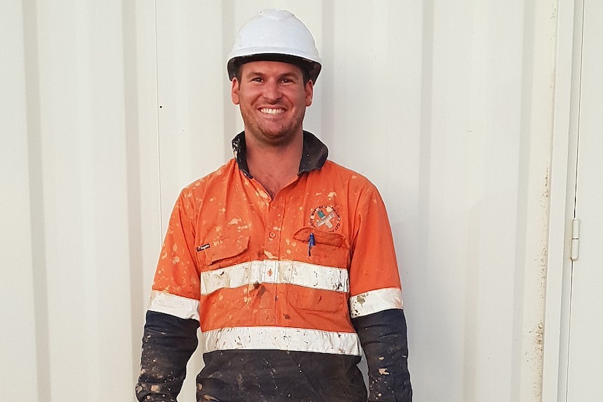 A man wears a white helmet, an orange top and blue pants