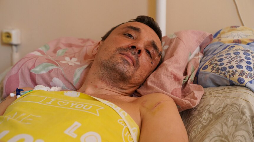 A man lying in a hospital bed looks down at the camera.