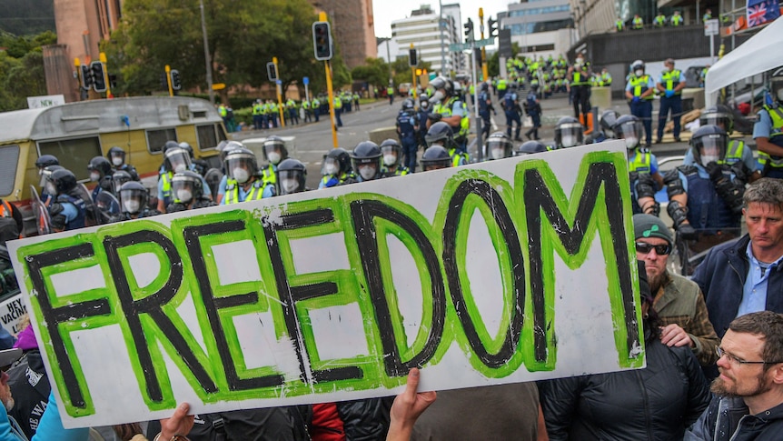 A white poster that has green text stating 'Freedom' in front of police.