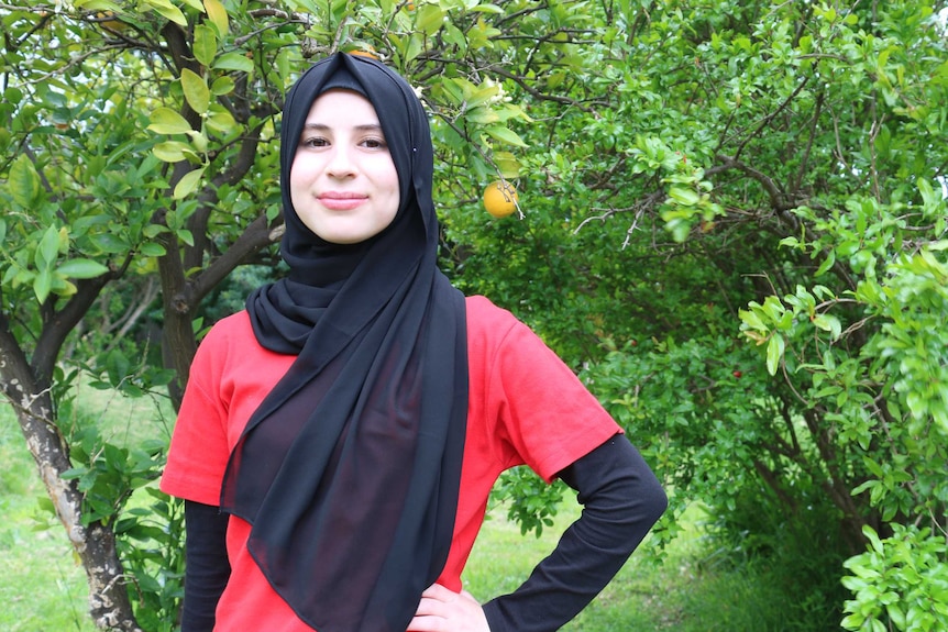 A young woman in a red shirt standing in front of a fruit tree