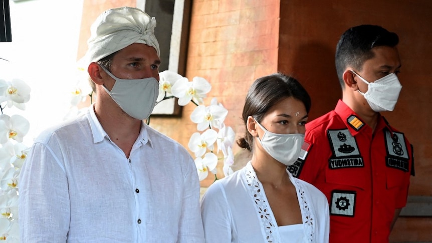 A Russian man and woman in traditional Balinese attire stand next to an official