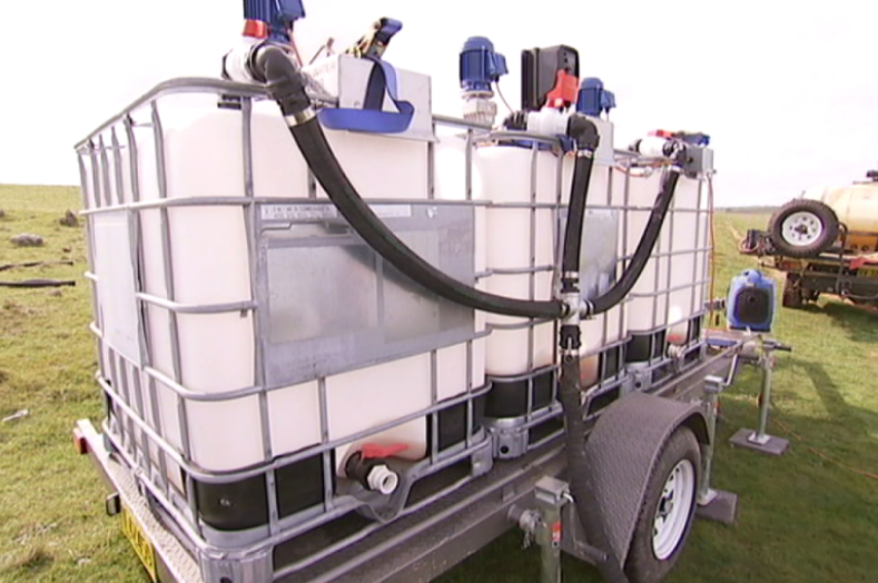 Three 1,000 litre water containers on a trailer with pipes coming off it.