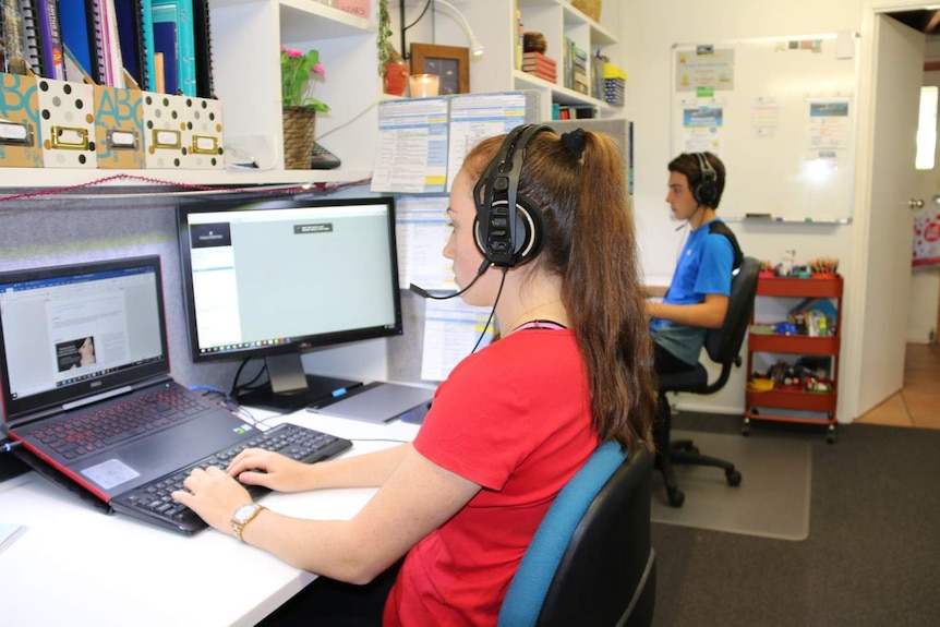 Distance education high school students Sophie and Harry Steptoe sit at desks on computers wearing headsets.