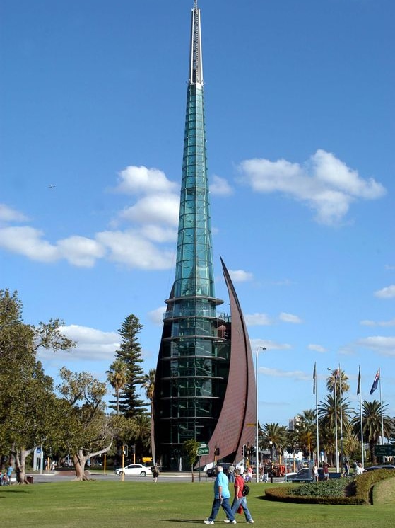 Two people walk past the bell tower of the Swan Bells