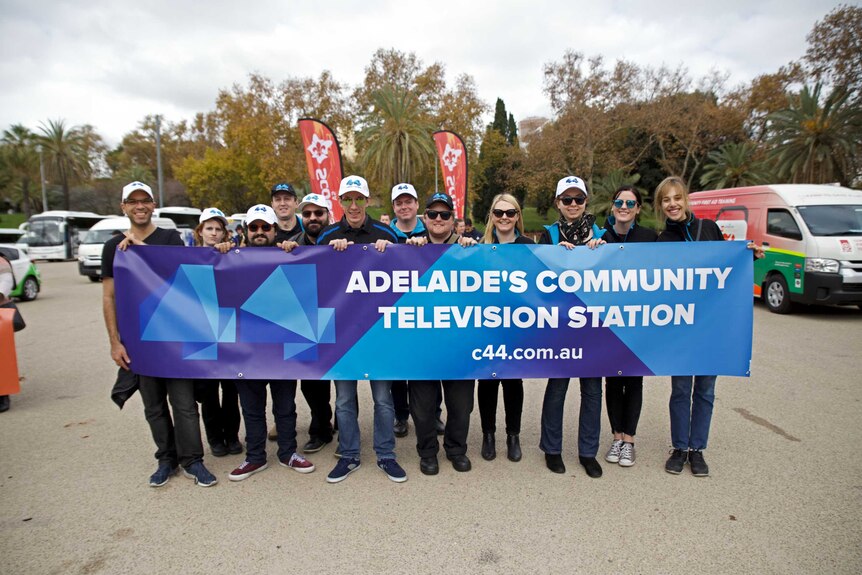 12 community television volunteers and staff hold up a banner that reads 'Adelaide's Community Television Station'