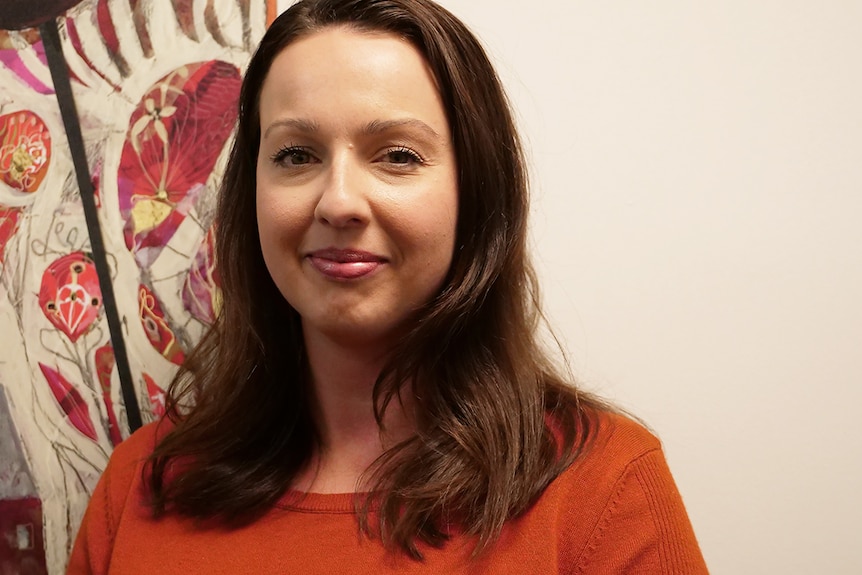 Miranda Batchelor smiling in front of a colourful painting.