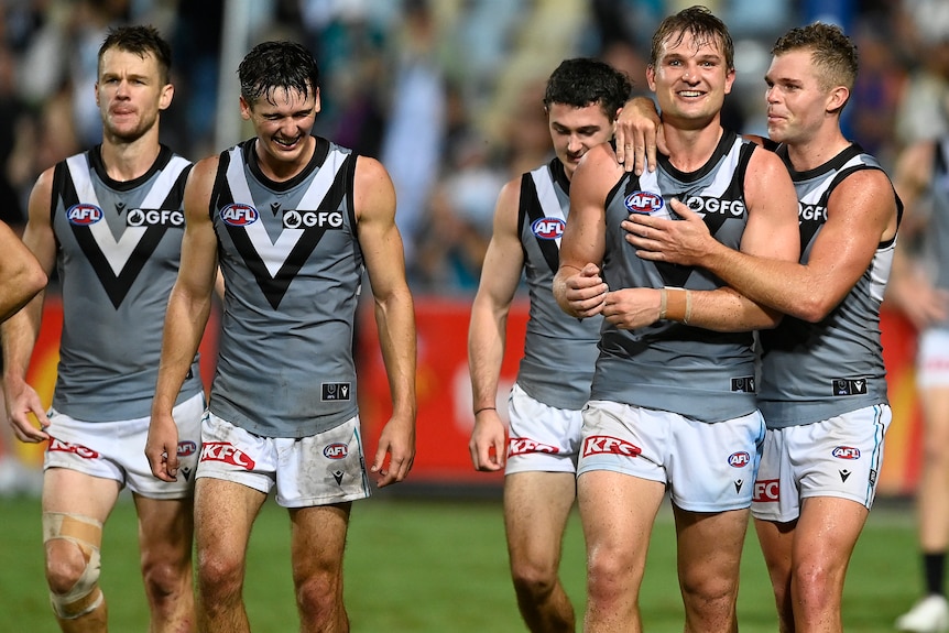 Port Adelaide players including Connor Rozee and Ollie Wines smile as they walk off the field