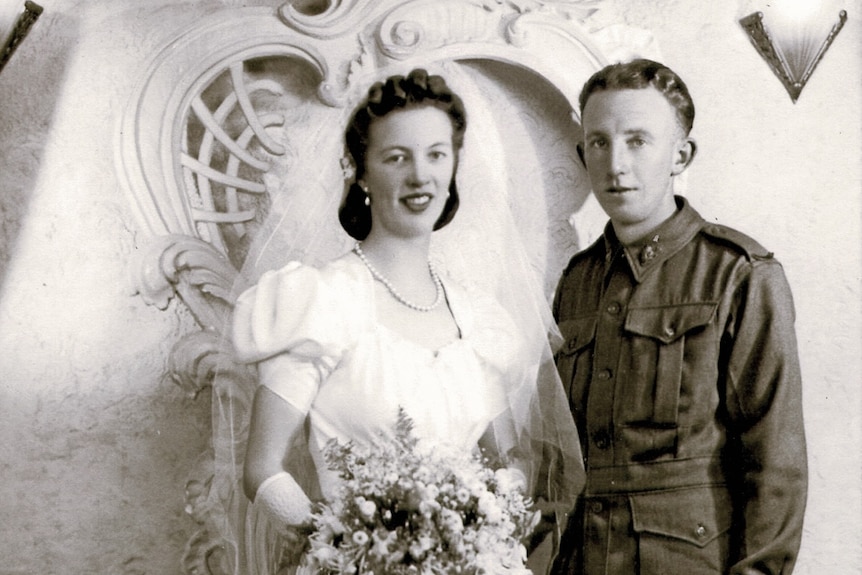 A black and white photo of a bride in a veil and wedding gown next to a man in army uniform