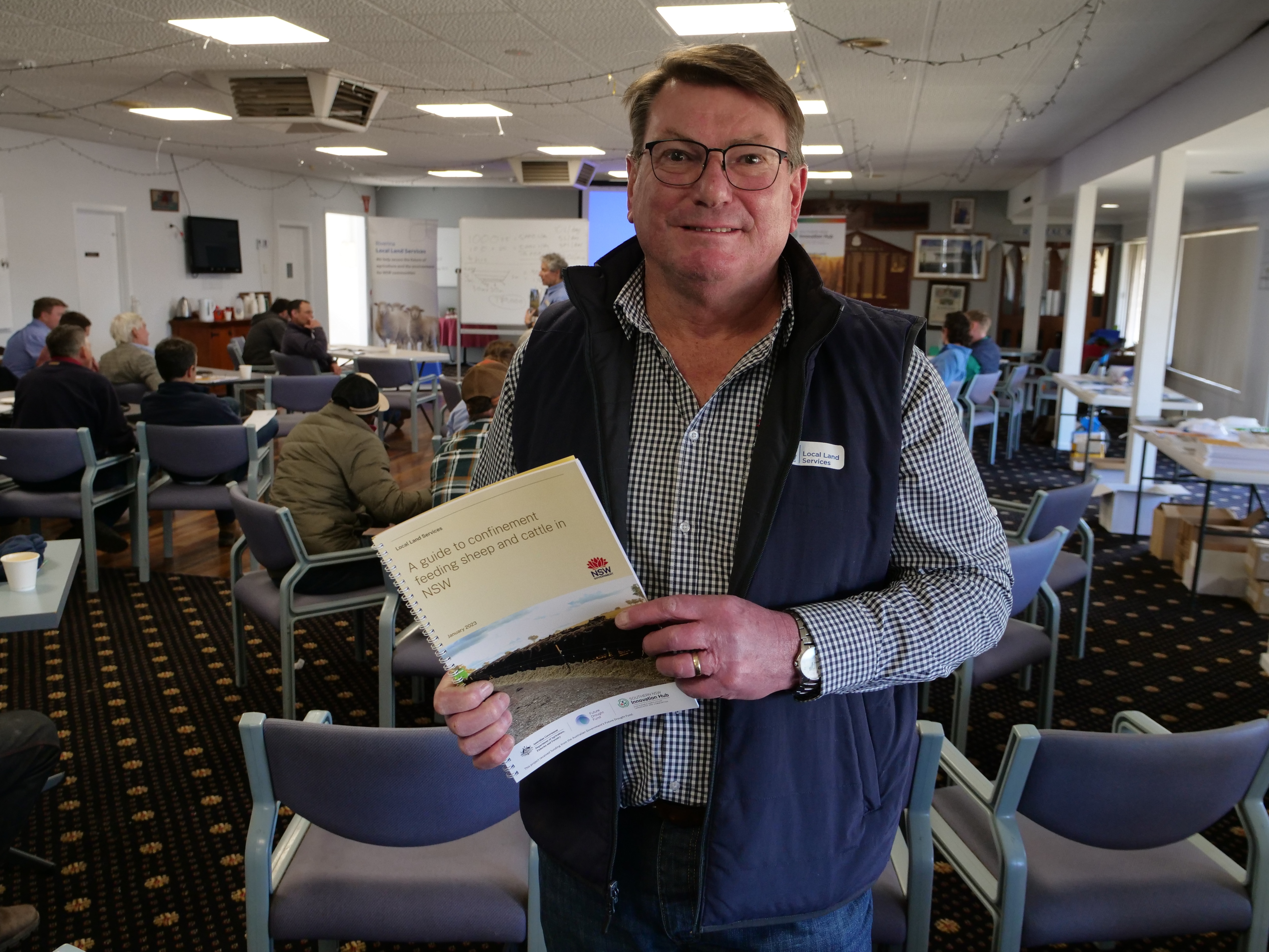 A man holding a book looks at the camera
