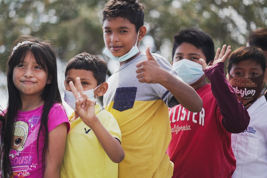 Five children wave to the camera and gives thumbs up and peace signs