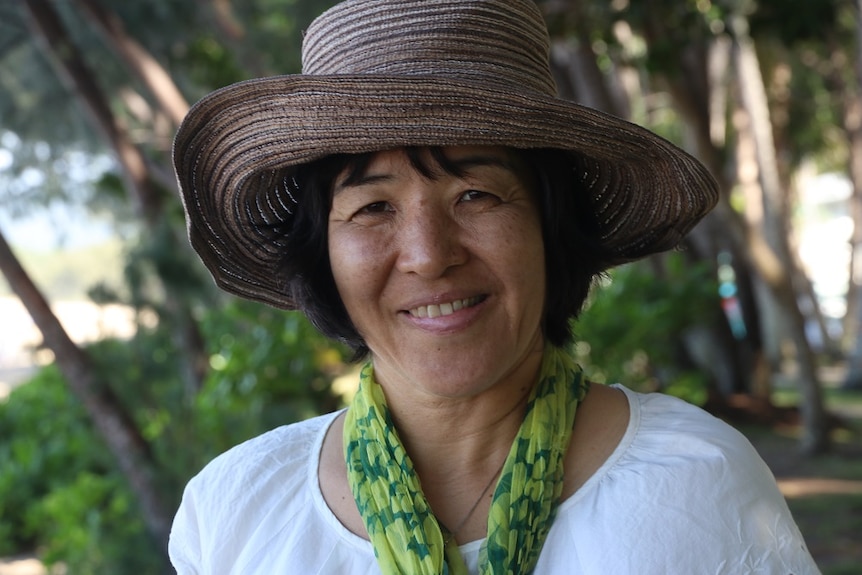 A smiling middle-aged woman wearing a hat and a loose green scarf.