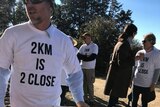 Man holding a protest sign saying two-kilometres is too close