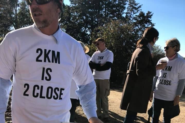 Man holding a protest sign saying two-kilometres is too close