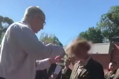 A video still of a man cutting a boy's hair, with the boy's face blurred so it he can not be identified.