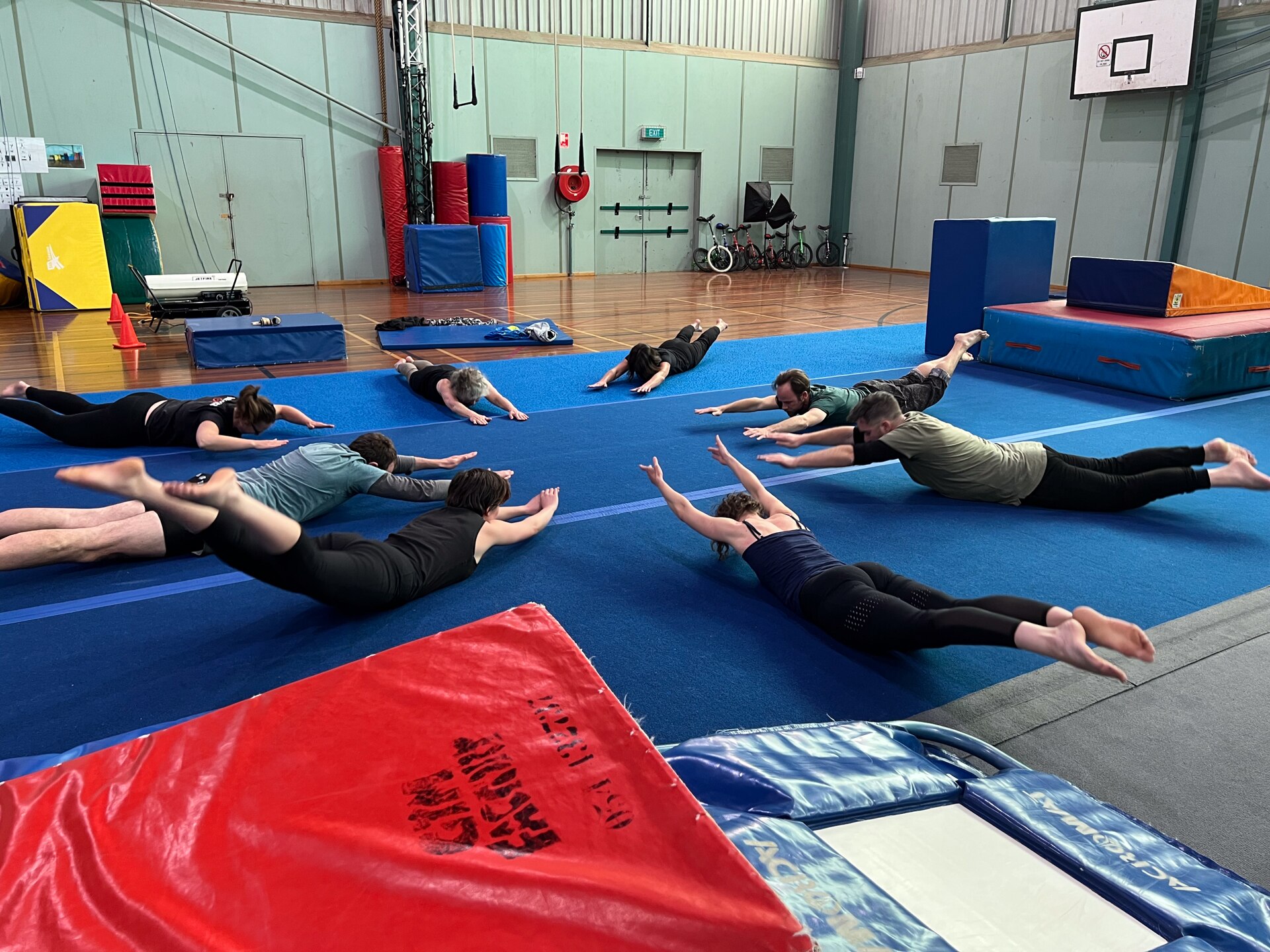 A group of people lying down on a blue gym mat with arms and legs stretched out