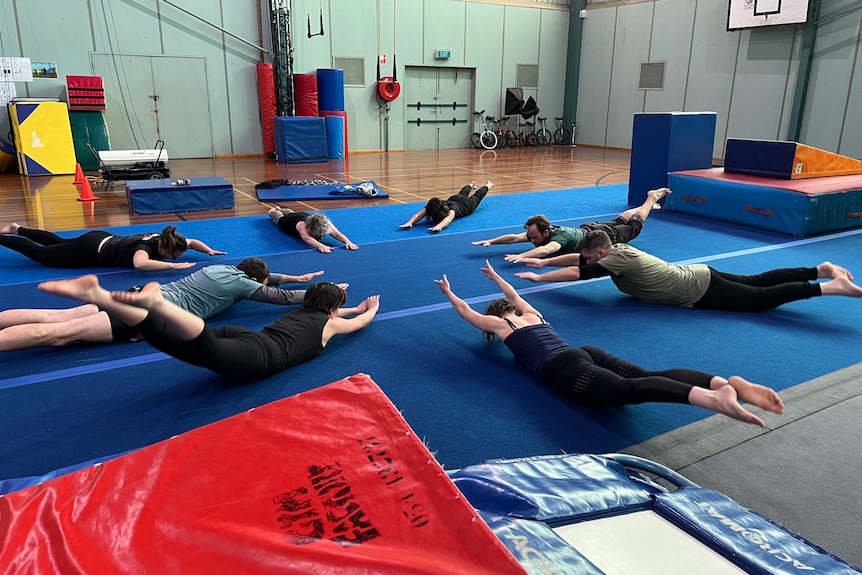 A group of people lying down on a blue gym mat with arms and legs stretched out