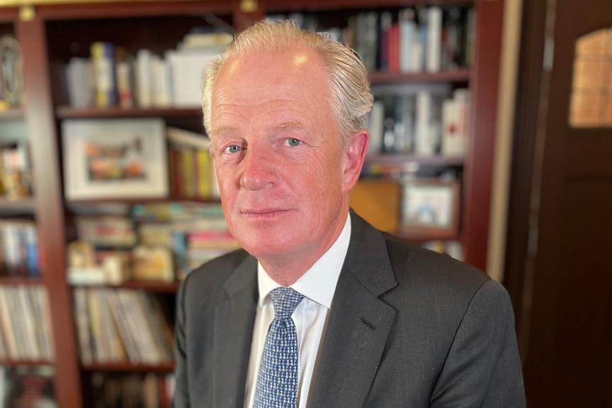 A man in a suit in front of a bookcase.