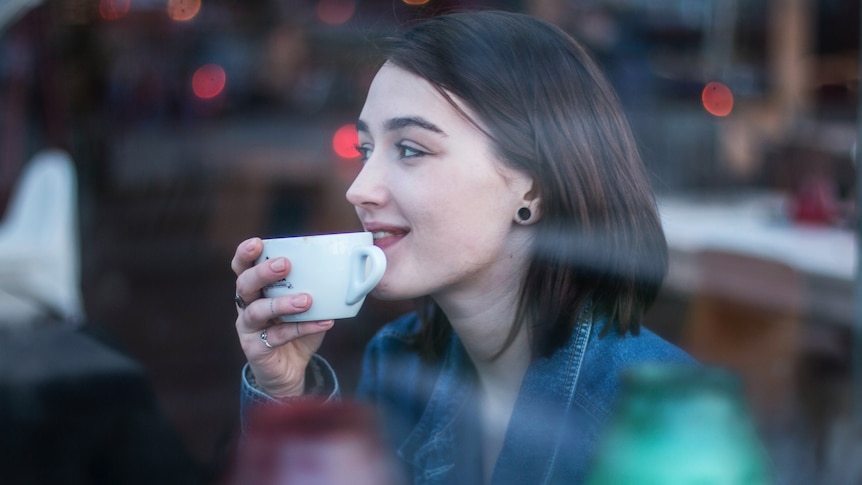Woman sits and enjoys a coffee, in a story about the guilt of changing hairdressers or coffee shops.
