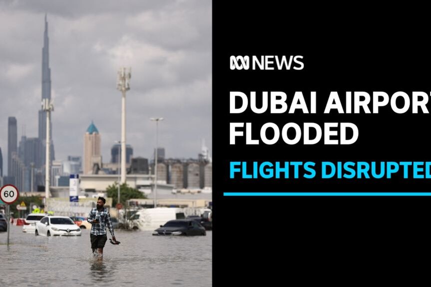 Dubai Airport Flooded, Flights Disrupted: A man walks along a flooded street holding his shoes. A cityscape in the background.