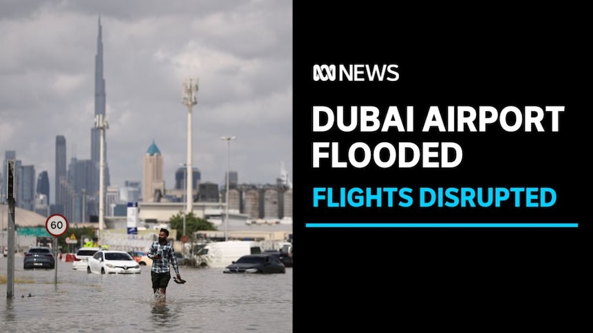 Dubai Airport Flooded, Flights Disrupted: A man walks along a flooded street holding his shoes. A cityscape in the background.