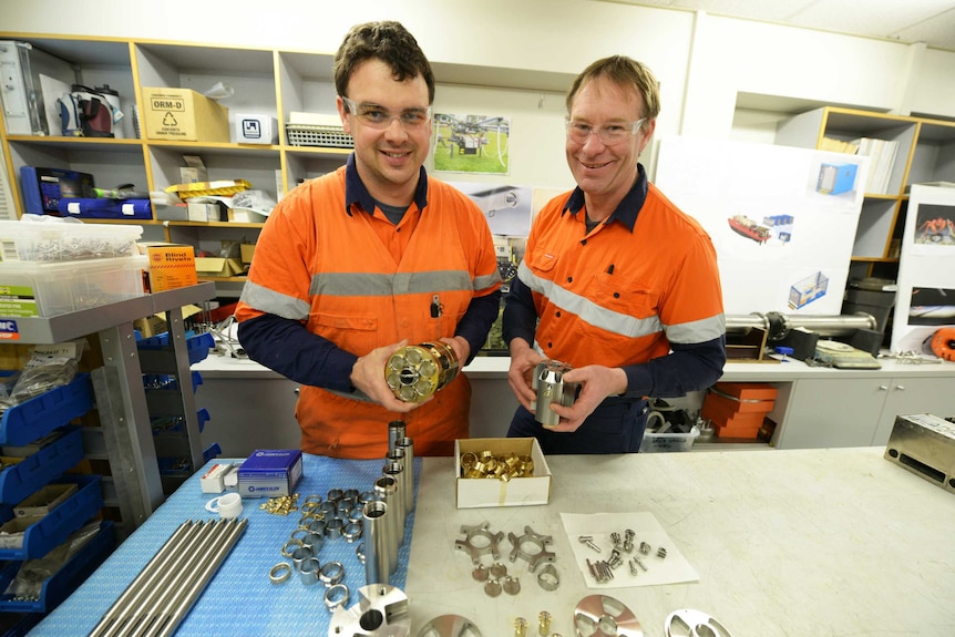 Two AAD employees in high-vis gear hold parts of an ice core drill
