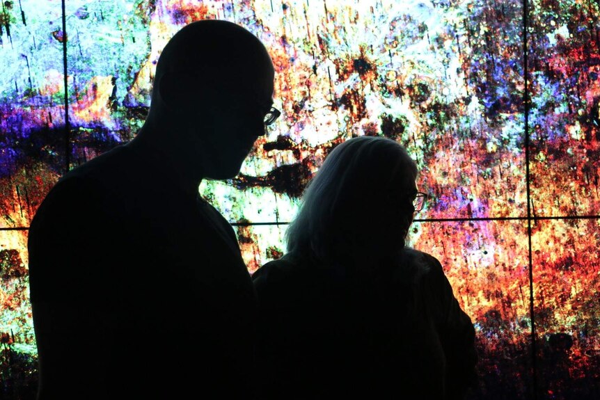 Two people silhouetted against a colourful image of Mars.