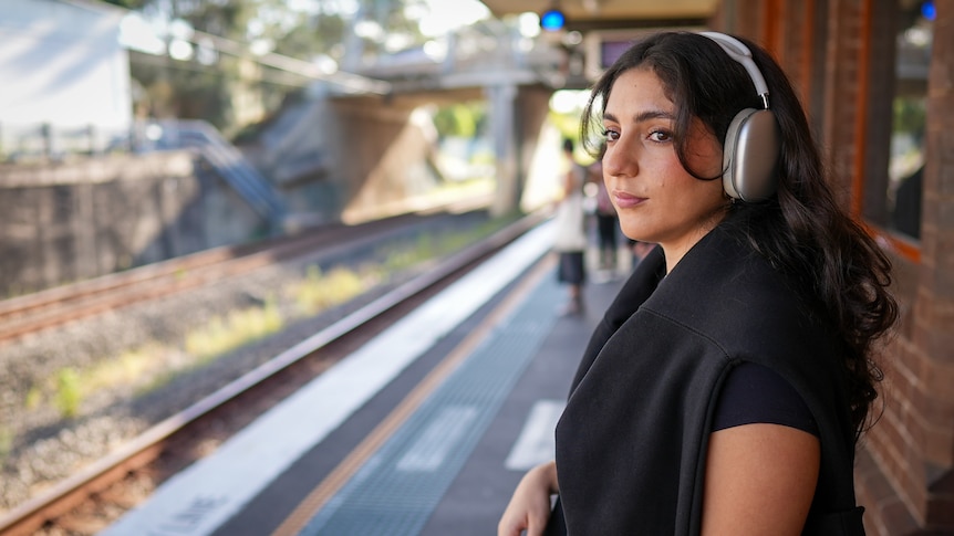 Afsoun Rastegari wearing headphones and looking into the distance at a train station.