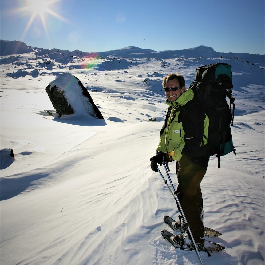 Man in snow gear in a snowscape with low sun in background.