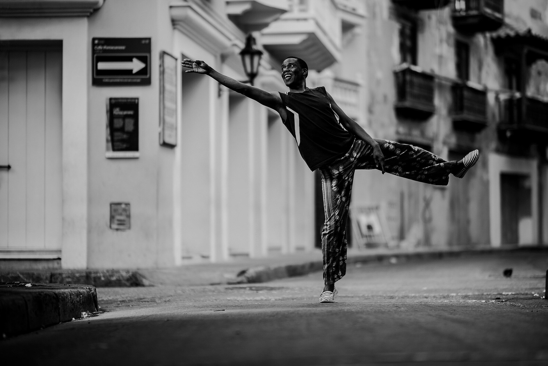 Person performing a dance pose on an empty street, standing on one leg with the other extended behind.