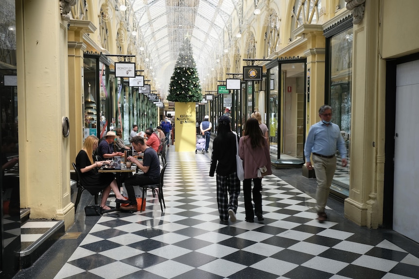 Shoppers both seated and walking in a Melbourne arcade with a Christmas tree in the background.