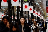 People walking along a street in Tokyo lined with Japanese flags.
