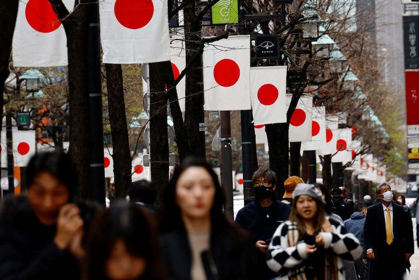日本の国旗が並ぶ東京の街を歩いている人々。